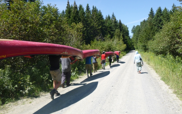 a group of people portage canoes a long a road